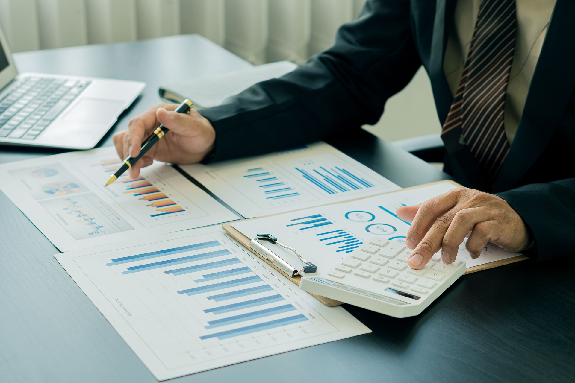 Un homme d’affaires appuie sur une calculatrice blanche pour calculer des chiffres dans les documents financiers de l’entreprise. Le service financier prépare des documents comptables, analysant les revenus et les dépenses de l’entreprise.